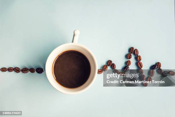 Silhouette of a steaming cup of coffee made up of coffee beans on a orange background.